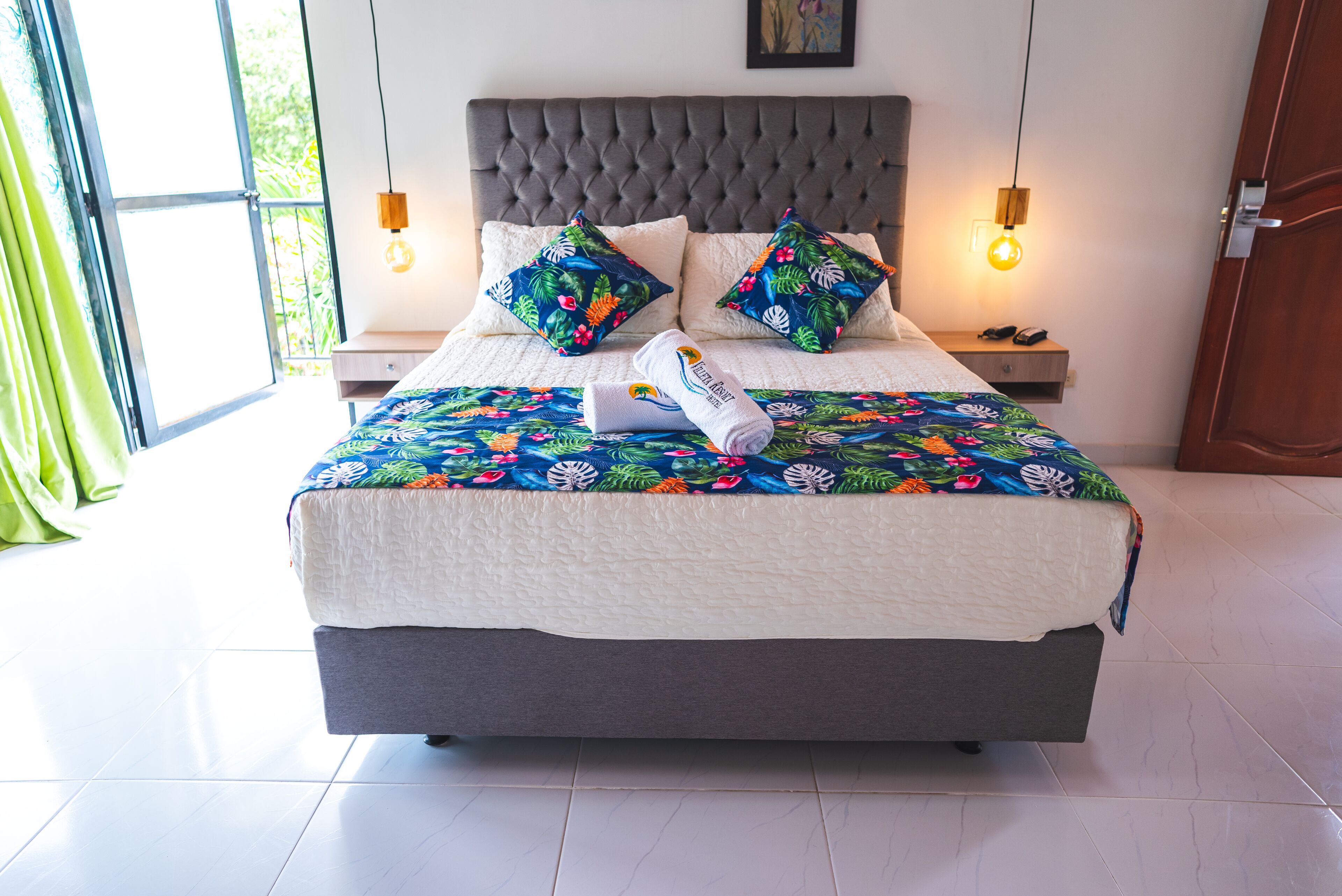 A neatly made bed with a floral bedspread, two decorative pillows, and a folded towel on the side.