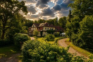 A large house surrounded by lush greenery, with a cobblestone path leading to the entrance. - Seegut Blaue Blume (Boitzenburger Land)