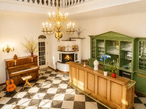 Een kamer met een weelderige kroonluchter, een piano, een open haard en een groene kast met drinkglazen.
