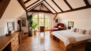 A bedroom with a large bed, wooden floor, a chair, a table, and a window. - Seegut Blaue Blume (Boitzenburger Land)