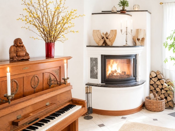 A corner room with a piano, a fireplace, a Buddha statue, and a vase with yellow flowers.