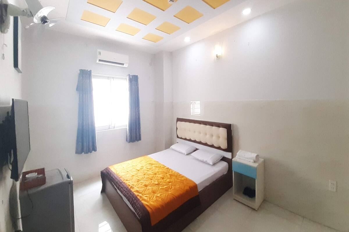 A hotel room with a bed, a nightstand, a TV, and an air conditioning unit.