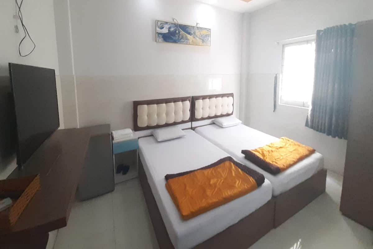 A hotel room with two beds, a flat-screen TV, a desk, and a window with curtains.