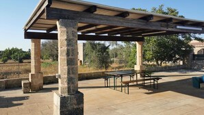 Un pavillon extérieur doté de colonnes en pierre et d’un toit en bois, comprenant des tables de pique-nique et un barbecue.