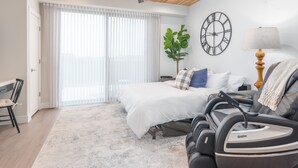 Un dormitorio con una cama, una silla de masaje, un reloj y una planta.