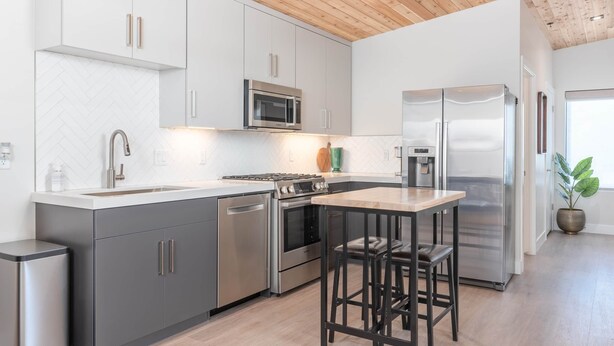 Una cocina moderna con electrodomésticos de acero inoxidable, gabinetes grises y techo de madera.