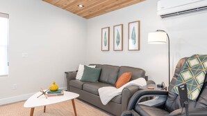 Una sala de estar moderna con un sofá de cuero, un sillón de masaje, una mesa de centro blanca e impresión botánica enmarcada en la pared.