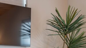 Un salon moderne avec un banc en bois foncé, un grand panier en osier contenant une plante et un téléviseur à écran plat fixé au mur.