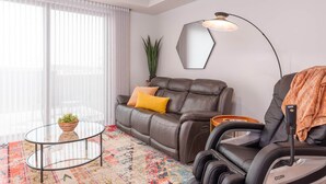 Un salon moderne avec un canapé en cuir, un fauteuil massant, une table basse en verre et un grand miroir.