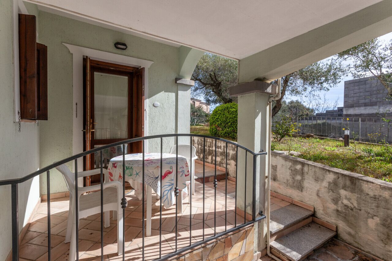 A covered outdoor area with a table and chairs, a door, and a view of the surrounding area.
