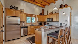Una cocina moderna con armarios de madera, electrodomésticos de acero inoxidable y una isla central con taburetes de bar.