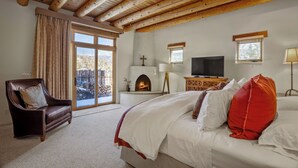 Un dormitorio con una cama grande, techo de madera, chimenea, televisor y vistas al exterior.