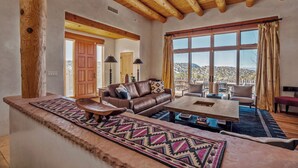 Un salón amplio con un gran ventanal, vigas de madera en el techo, un sofá de cuero y una mesa de centro.