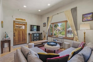 Uma sala de estar com porta de madeira, televisão, um banco e um sofá.