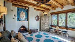 A cozy room with a fireplace, a bed with a patterned bedspread, a wooden ceiling, and a view through large windows.