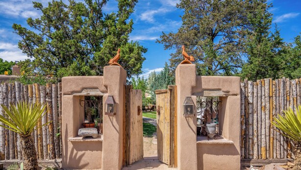 A rustic gate with a wooden fence, a clear sky, and a pathway leading into a garden area.