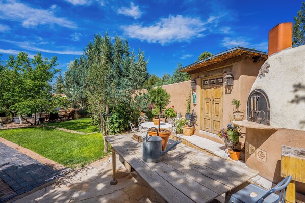 A patio with a wooden table, a metal watering can, and potted plants.