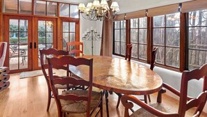 A dining area with a wooden table and chairs, large windows with a view of trees, and a chandelier. - Casa Segunda | Elegant Santa Fe Retreat (Santa Fe)