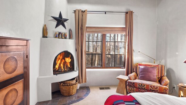 A cozy room with a fireplace, a window with curtains, a patterned bedspread, and a star decoration on the wall. - Casa Segunda | Elegant Santa Fe Retreat (Santa Fe)