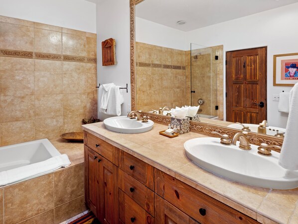 Un baño con dos lavabos, una bañera, armarios de madera y un espejo grande.