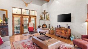A spacious living room with a fireplace, a large window, and a wooden ceiling. - Casa Segunda | Elegant Santa Fe Retreat (Santa Fe)