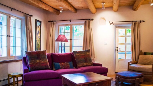 A cozy living room with a purple sofa, wooden coffee table, and a patterned rug. - Casa del Monte Sol | Charming Adobe Retreat (Santa Fe)