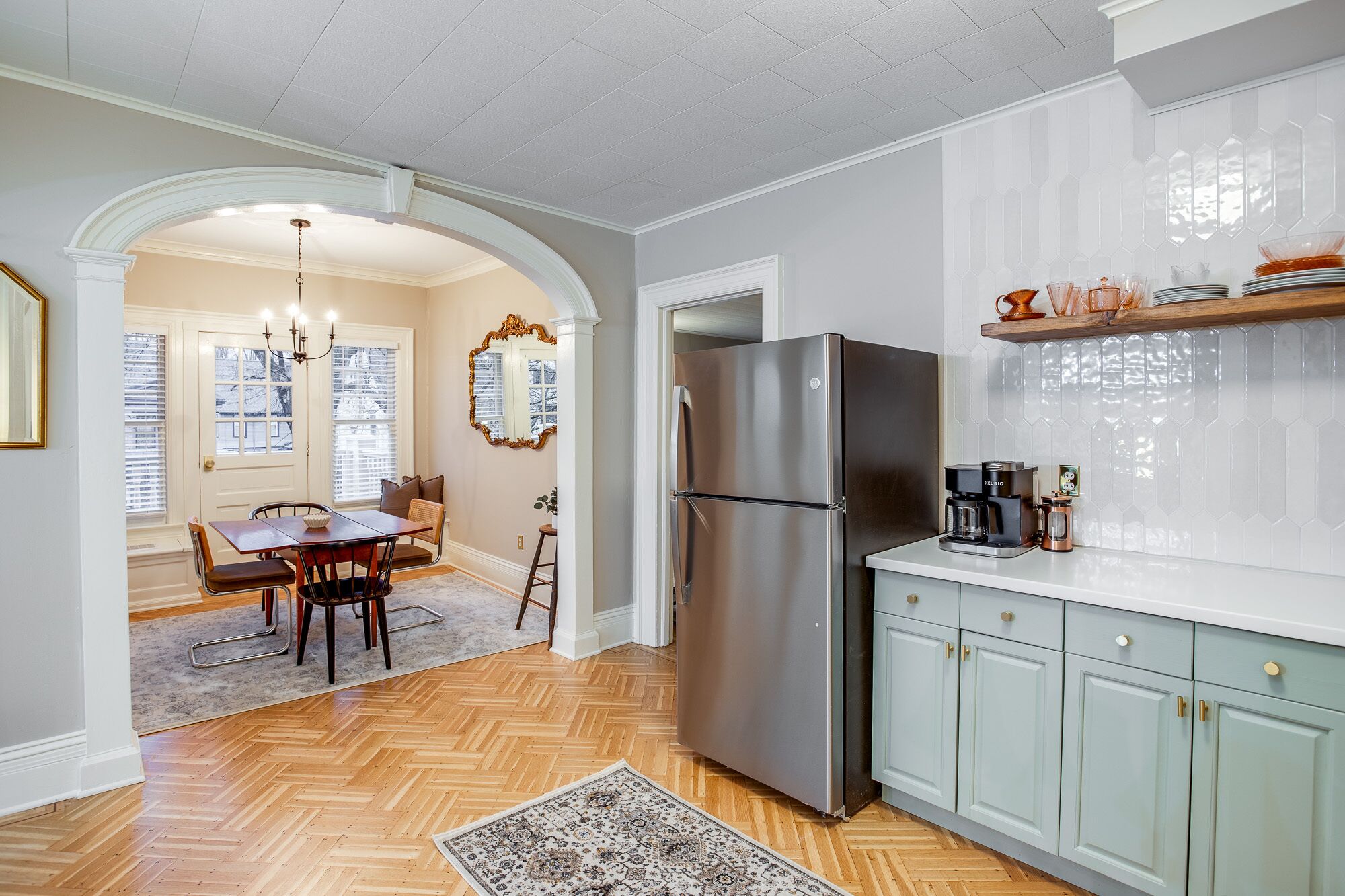 A kitchen with a stainless steel refrigerator, a coffee maker, and a patterned rug on the floor.