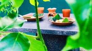 A table with terracotta pots and a small clay pot with a lid, possibly for holding food or drink, set against a dark background with green foliage in the foreground. - Marian Villa Katunayake  (Seeduwa - Katunayake)