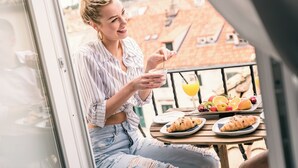 A person sitting at a table with a meal and drinks on a balcony.