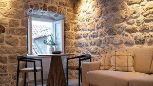 A cozy room with a stone wall, a wooden table with two chairs, a sofa, and a bowl of fruit on a small table.