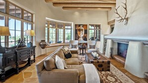 A spacious living room with a fireplace, large windows, and a cozy seating area. - Villa Campanas | Luxury Home with Mountain Views (Santa Fe)