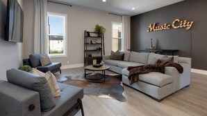 A modern living room with a grey sofa, a coffee table, and a bookshelf. - 2 Lux Homes, 8 bedrooms/28 beds! Baller Game Room (Nashville)