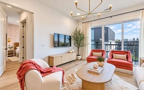 Ein modernes Wohnzimmer mit großem Fenster, einem Flachbildfernseher, einem Couchtisch aus Holz und zwei roten Sesseln.