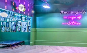 Ein Zimmer mit Türkiswänden, einem Neon-Schild mit der Aufschrift „Pour myself a cup of ambition“ und einem Schild mit der Aufschrift „Going Up“.