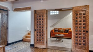A spacious room with a wooden floor, a staircase, and a cozy orange sofa with patterned cushions.