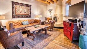 A cozy living room with a wooden ceiling, a large rug, a leather sofa, a wooden coffee table, and a red dresser.