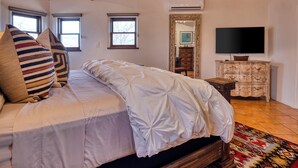 A bedroom with a wooden ceiling, a bed with white bedding, a television, and a dresser.
