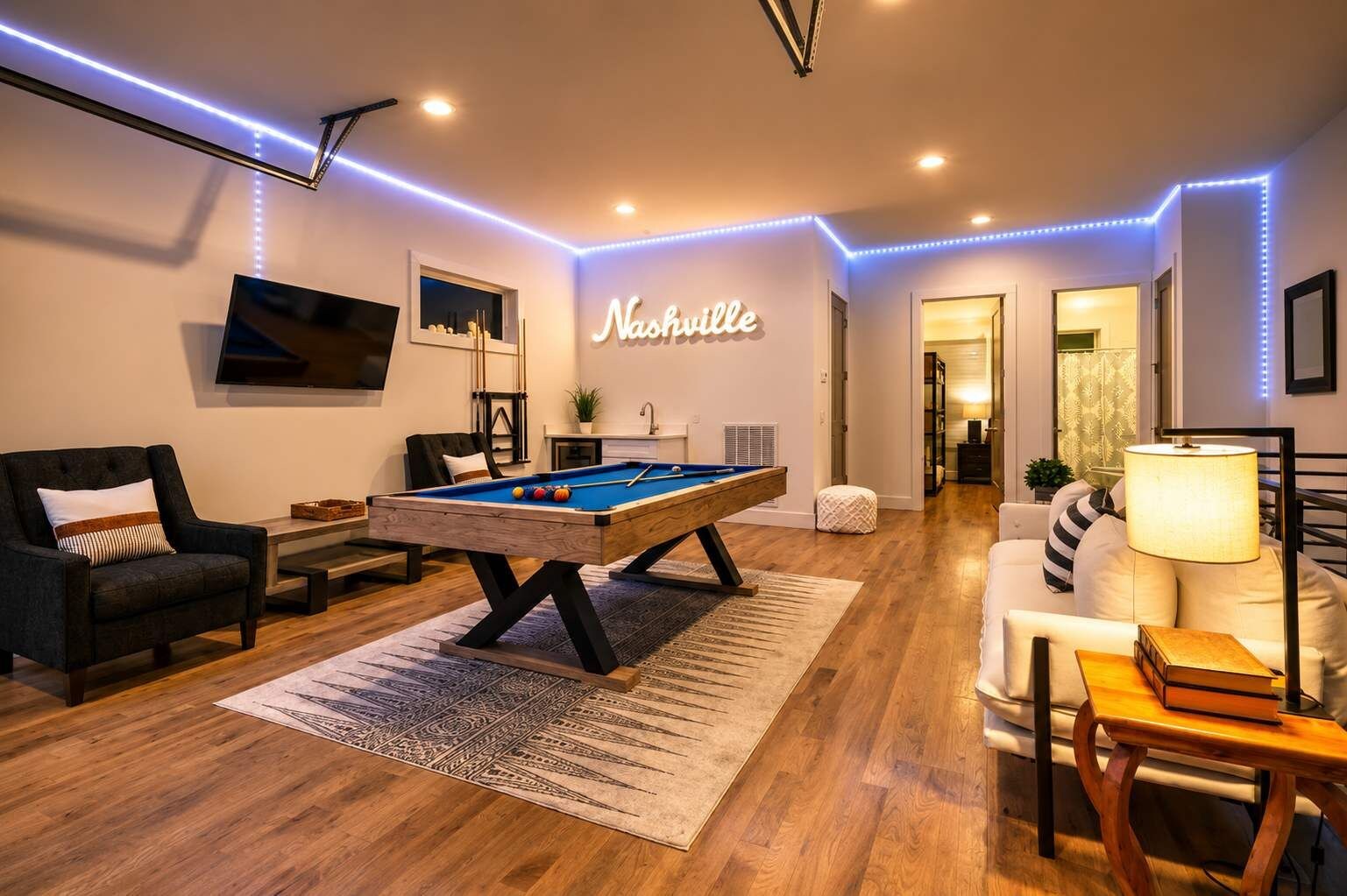 Een moderne woonkamer met een pooltafel, een bank, een televisie en een trap naar een andere kamer.