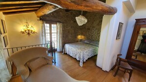 A rustic bedroom with a wooden ceiling, a bed with a patterned bedspread, a nightstand, a chair, and a chandelier.