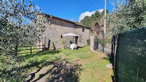 A stone building with a rustic exterior, a fenced yard, and a table with chairs under an umbrella.