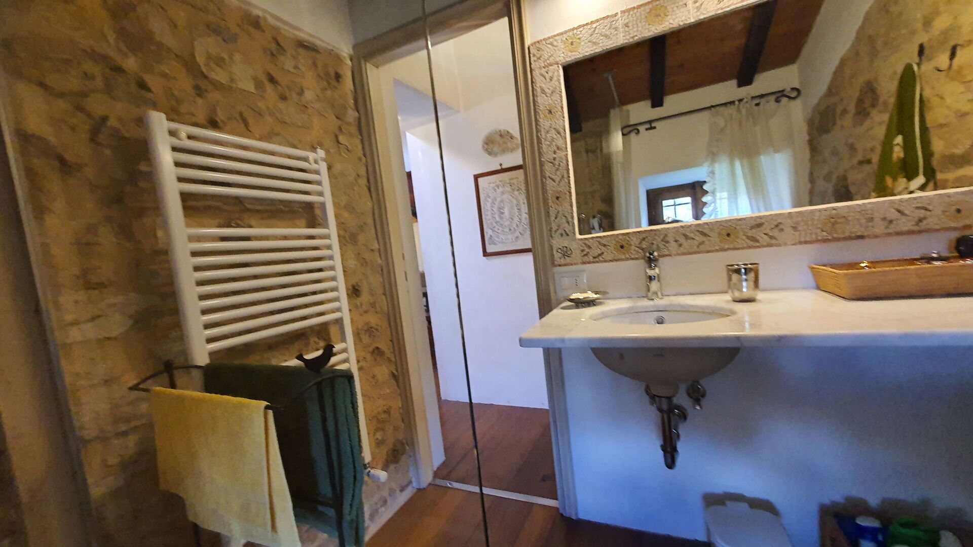 Un baño con pared de piedra, toallero blanco, lavabo y espejo con marco decorativo.