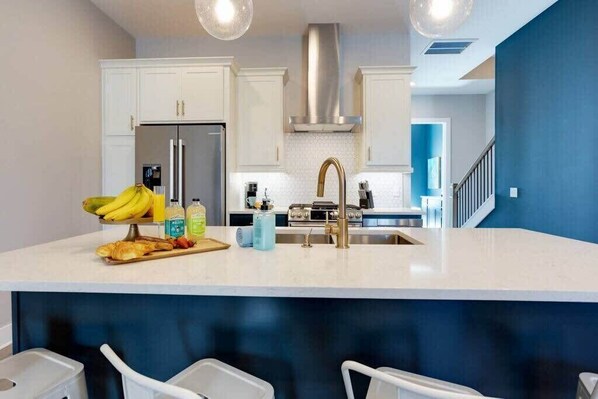 A modern kitchen with white cabinetry, stainless steel appliances, and a central island with a sink and bar seating.