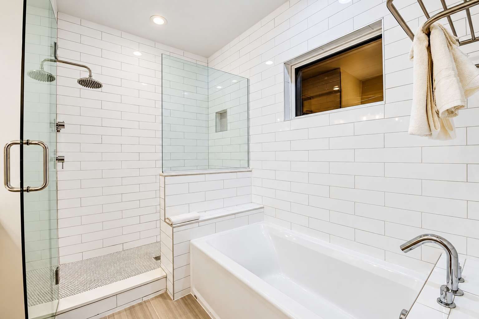 A modern bathroom with a glass-enclosed shower, a bathtub, and a window above the sink.