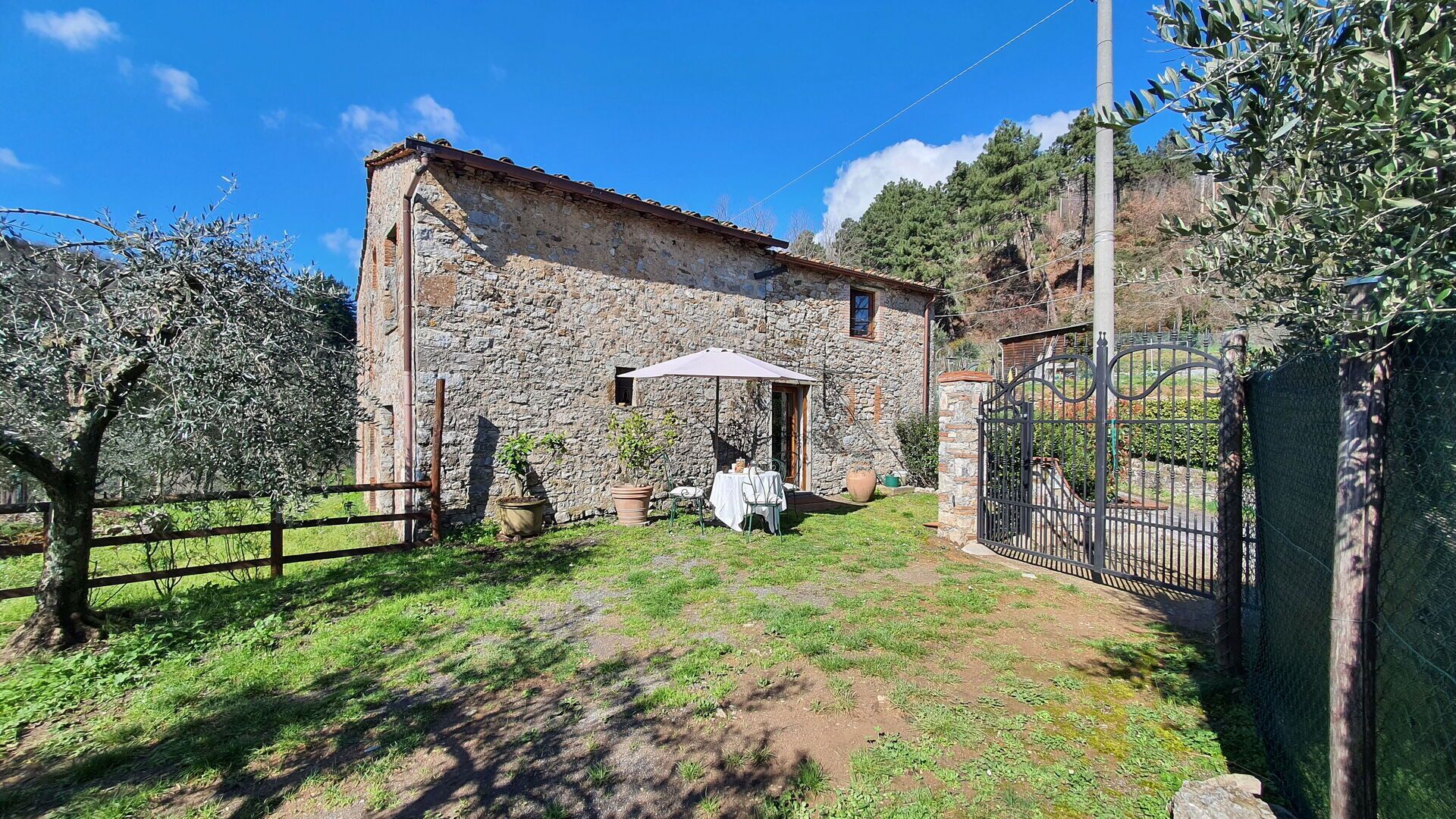 A stone building with a rustic exterior, a small patio with a table and chairs, and a metal gate.