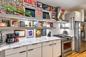 A kitchen with a stainless steel refrigerator, a gas stove, and a coffee maker. There are framed pictures and memorabilia on the wall. - Luxury Home Amazing Rooftop 11 Beds Pool Table! (Nashville)