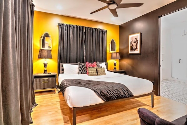 A bedroom with a bed, two bedside tables with lamps, a ceiling fan, a door, and a framed picture on the wall. - Luxury Home Amazing Rooftop 11 Beds Pool Table! (Nashville)