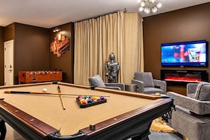 A billiards table with balls and cues, a foosball table, a statue, a television, and a seating area with chairs. - Luxury Home Amazing Rooftop 11 Beds Pool Table! (Nashville)