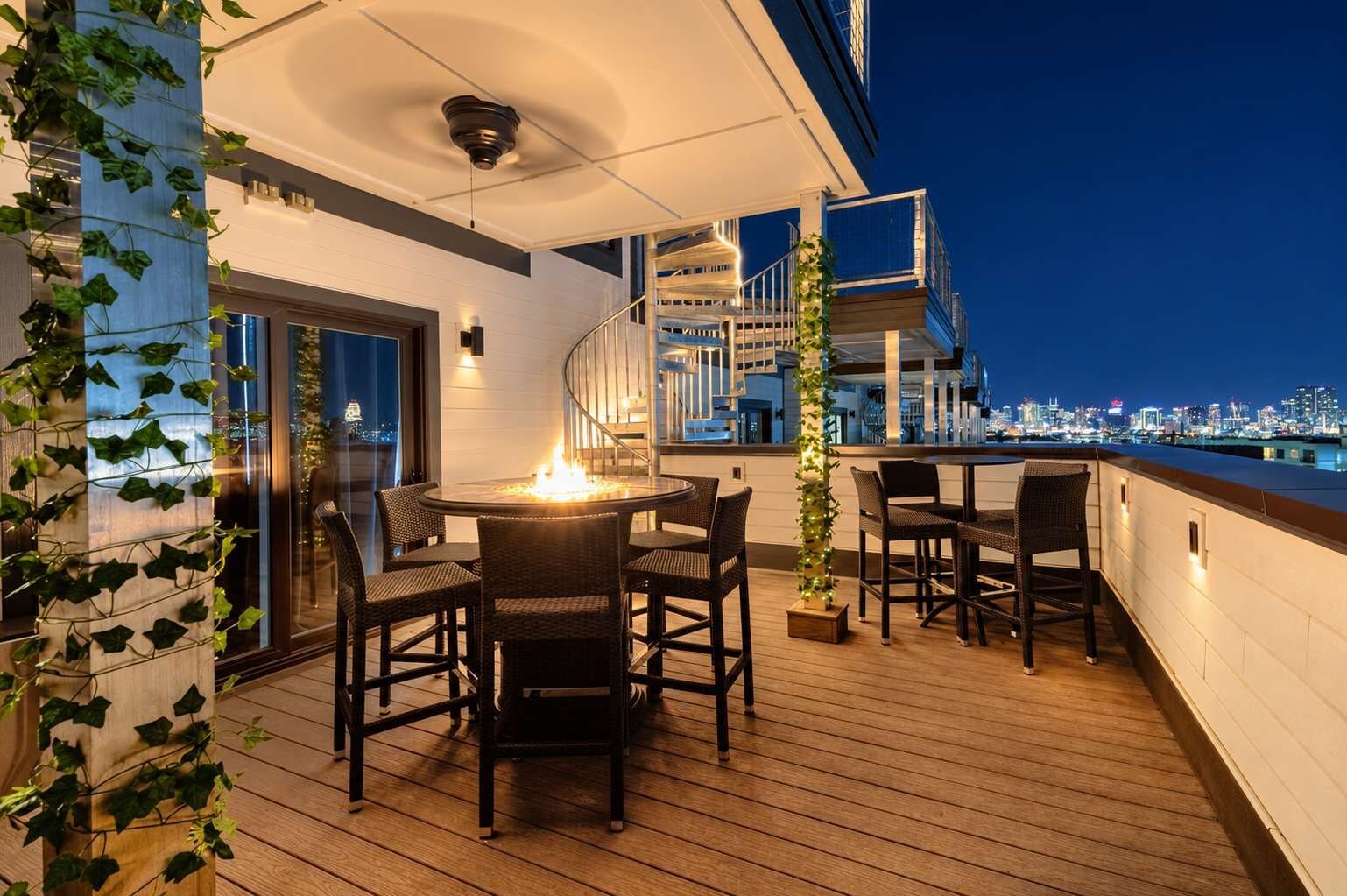 Terraza en la azotea con mesa y sillas redondas, una chimenea y vistas nocturnas del horizonte urbano.