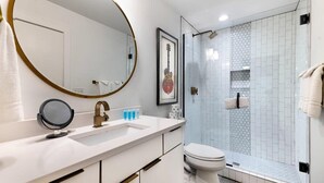 Een moderne badkamer met een witte wastafel, een ronde spiegel, een ingelijste gitaar en een douchecabine met zeshoekig tegels.