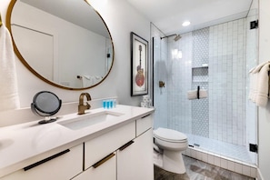 A modern bathroom with a white vanity, a round mirror, a framed guitar, and a glass-enclosed shower with hexagonal tiles. - Luxury Home Amazing Rooftop 11 Beds Pool Table! (Nashville)